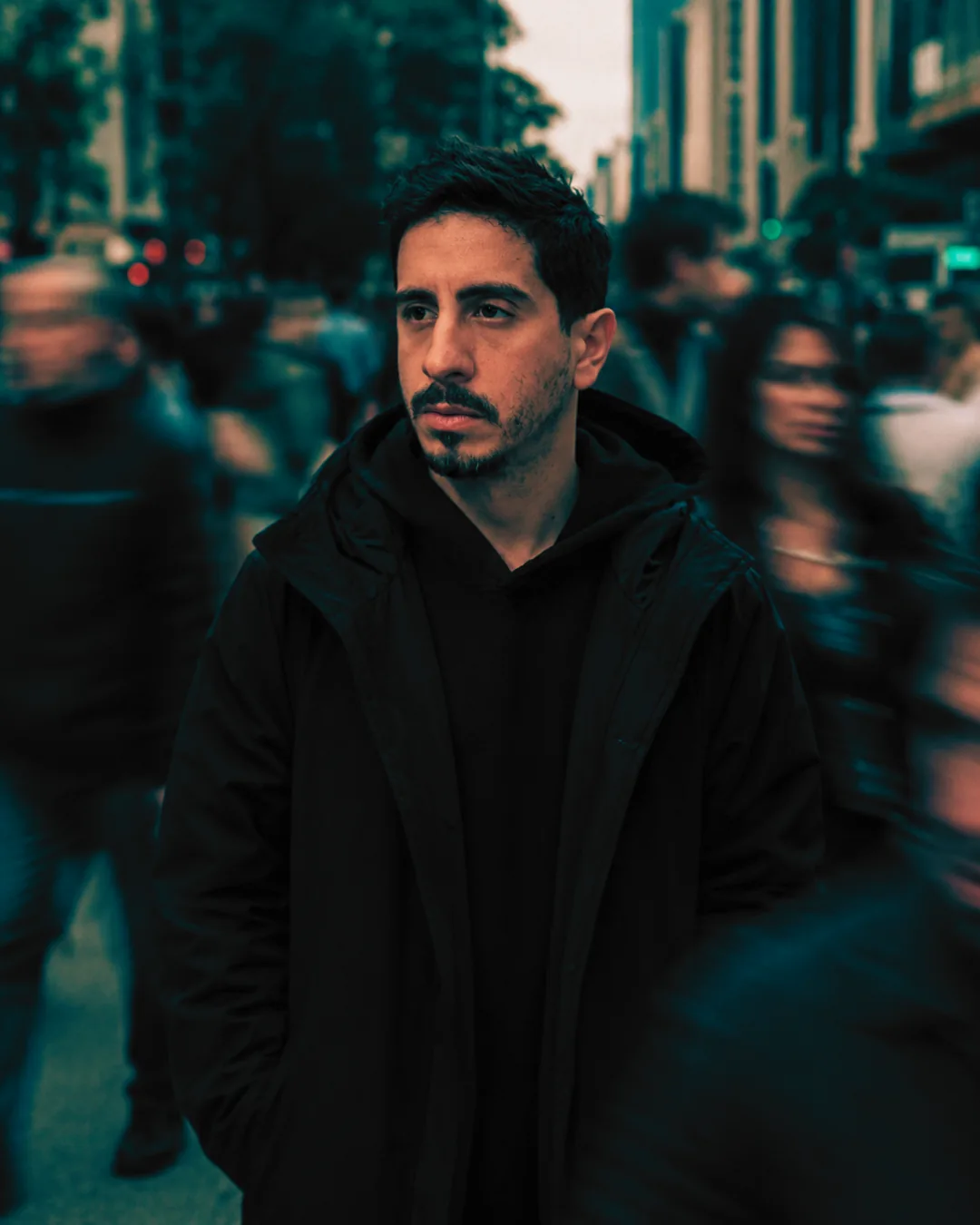 Thiago Damasceno, fundador da ALQUIM_IA.LAB, parado em foco no meio de uma multidão em movimento